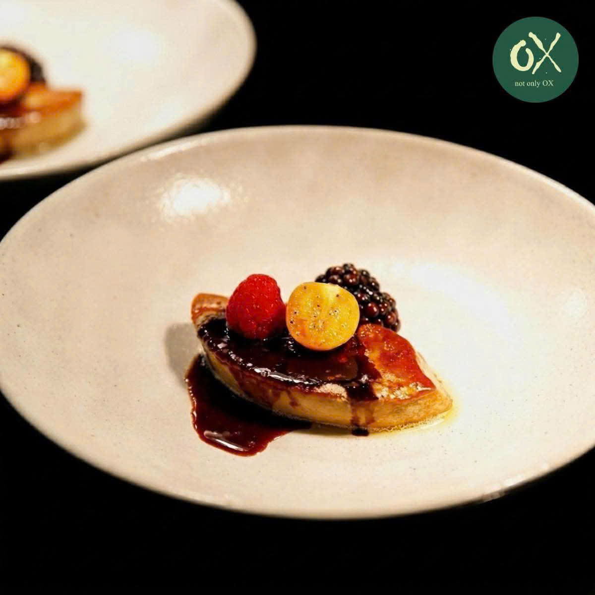 Seared foie gras with berries and dark sauce on a white plate